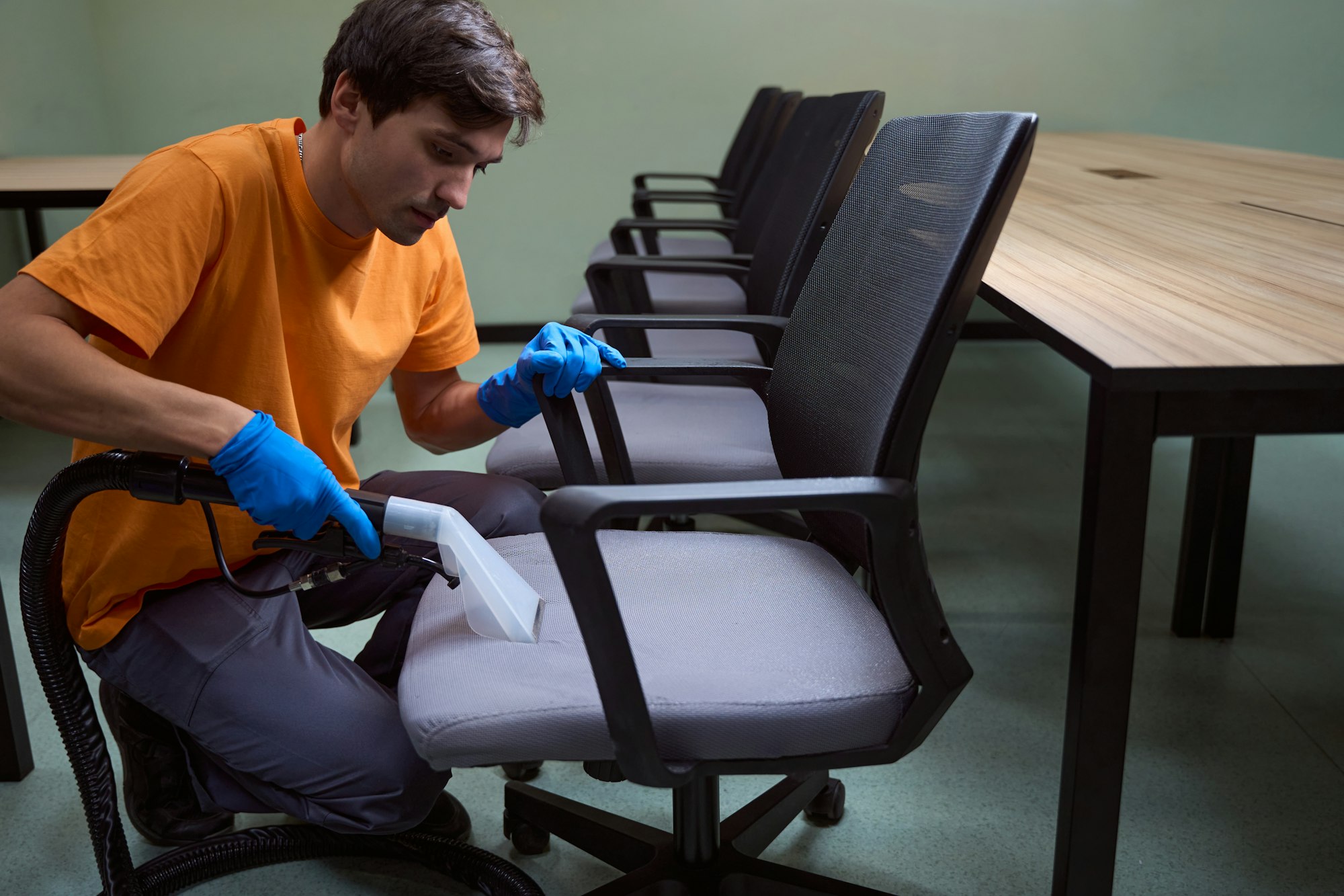 Hard-working janitor is deep-cleansing chairs with vacuum-cleaner